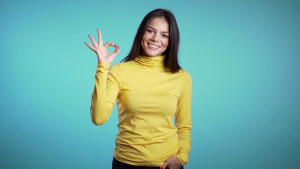Young woman making OK sign over blue background. Winner. Success. Positive brunette young hispanic girl smiles for camera. - Materiaali, video
