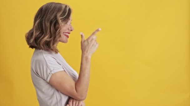 Positive young woman with red lips stands sideways and points a finger straight over yellow background isolated - Felvétel, videó