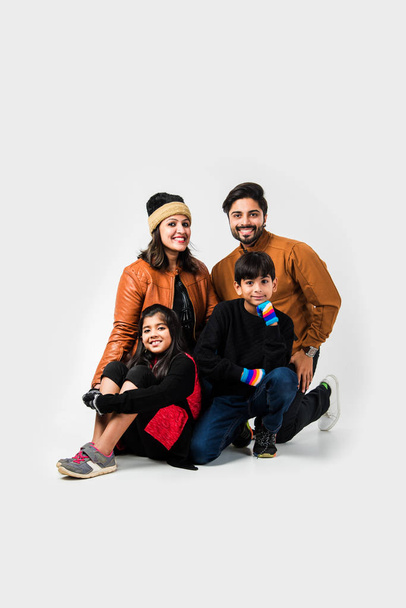 Familia india con ropa de abrigo sentada sobre fondo blanco. Listo para el concepto de invierno - Foto, Imagen