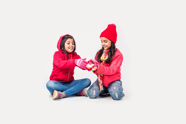 Twee Indiase kleine meisjes in warme kleren tegen witte achtergrond - Foto, afbeelding