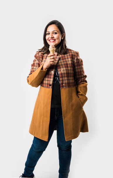 Indian woman eating ice cream while wearing warm winter clothes on white background - Photo, Image