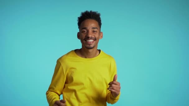 Young african american man smiling and dancing in good mood on blue background.Unstoppable fun, happiness, comical portrait of guy isolated. - Video