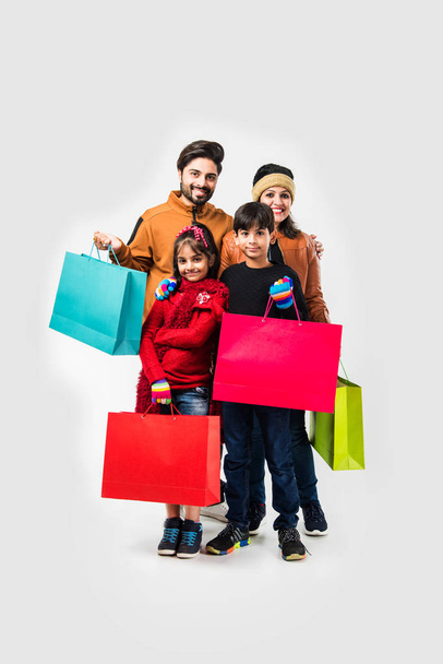 Indian family with shopping bags in winter warm clothes against white background - Photo, Image