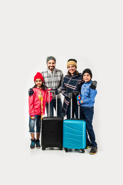 Retrato de estudio de la familia india con maletas mientras usa ropa de abrigo, listo para las vacaciones de invierno - Foto, imagen