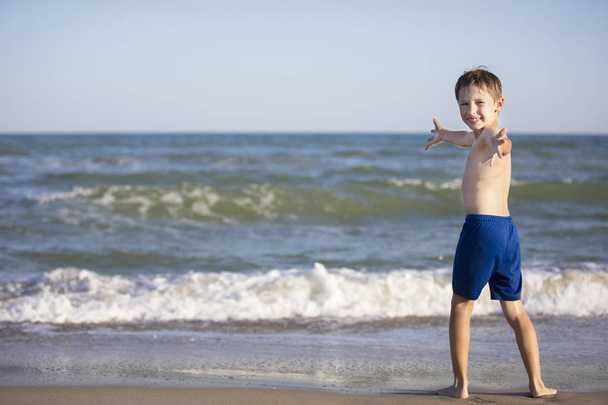 Gioioso ragazzo vicino al mare aprì le braccia. Bambino che riposa sulla spiaggia
 - Foto, immagini