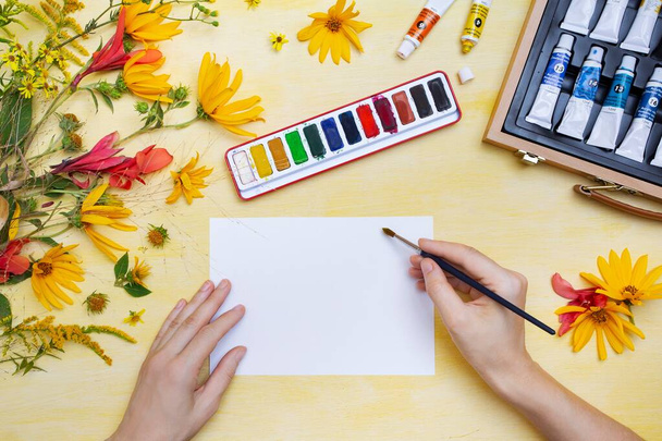 Person drawing on a white paper with watercolors on a wooden surface near colorful flowers - Fotoğraf, Görsel