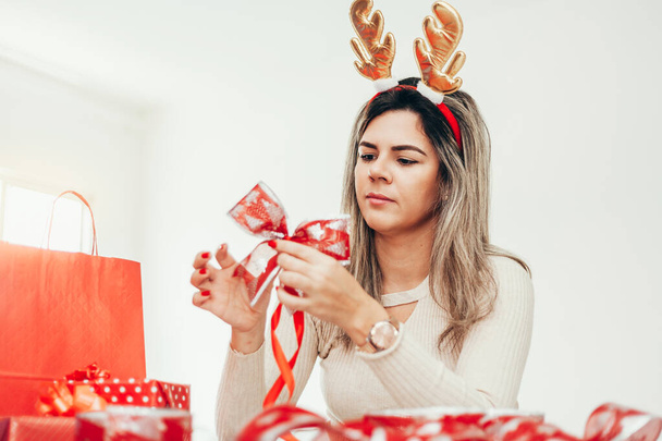 Christmas woman with reindeer horns headband preparing gifts wrapping paper for holidays - 写真・画像