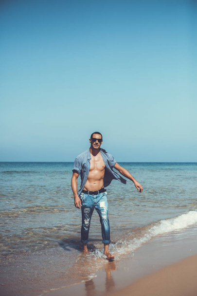 young muscular man resting and posing on the beach. A young man walks by the sea - Photo, Image