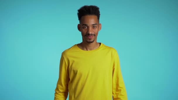 Handsome mixed race man in yellow wear on blue studio background smiles to camera and gives thumbs up. Happy guy showing gesture of approval. Winner.Success. - Πλάνα, βίντεο