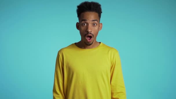 Amazed mixed race man shocked, saying WOW. Handsome african american guy with afro hair surprised to camera over blue background. - Materiał filmowy, wideo