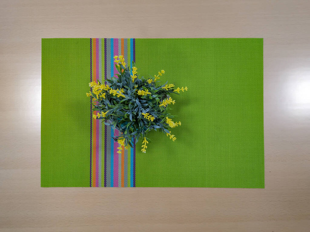 Masaya yerleştirilmiş yeşil masa örtüsü ve sahte sarı çiçekler. - Fotoğraf, Görsel