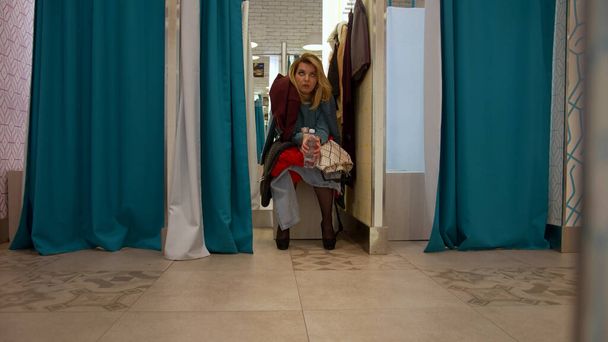 Young woman sits in the fitting room and is waits for something - Foto, afbeelding