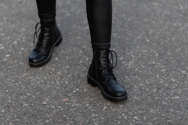 Modern young woman in black stylish leggings in fashionable leather boots stands on the road in the city. Trendy collection of women's autumn shoes. Close up of female legs. - Foto, imagen