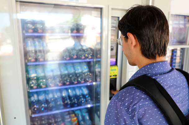 Joven mochilero turista masculino eligiendo un aperitivo o bebida en la máquina expendedora. Máquina expendedora con hombre
. - Foto, imagen