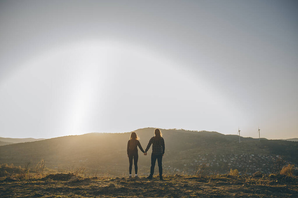 Young couple kissing on the background of a sunset in the field. Silhouette of a female and male holding hands at sunset. Couple holding hands. Couple of lover holding hand with sunrise - Photo, Image