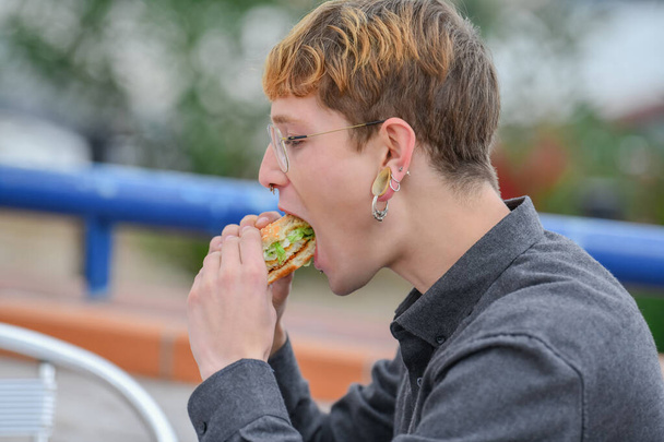 Ένας νεαρός άνδρας τρώγοντας ένα μπέργκερ - Φωτογραφία, εικόνα