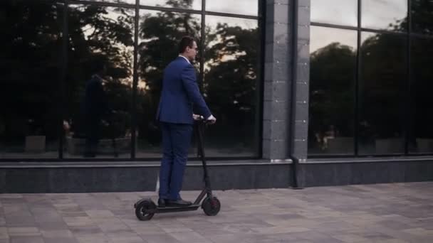 Young businessman riding an electric scooter for a business meeting in the office, office buildings, business man, electric transport, ecological transport. Side view - Imágenes, Vídeo