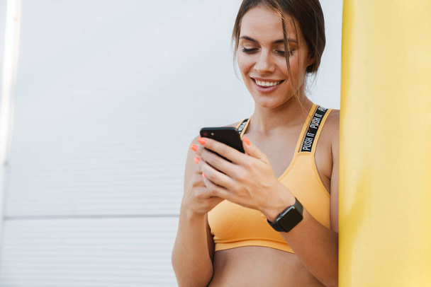 Image of happy woman in sportswear holding cellphone outdoors - Photo, image