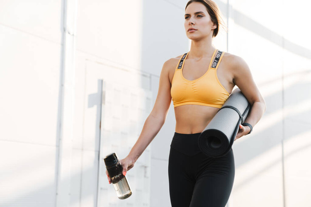 Image of lovely woman walking with yoga mat and water bottle out - Photo, Image