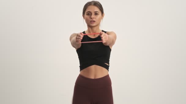 Sporty woman wearing tracksuit making exercises using expander fitness tape isolated over white wall - Felvétel, videó