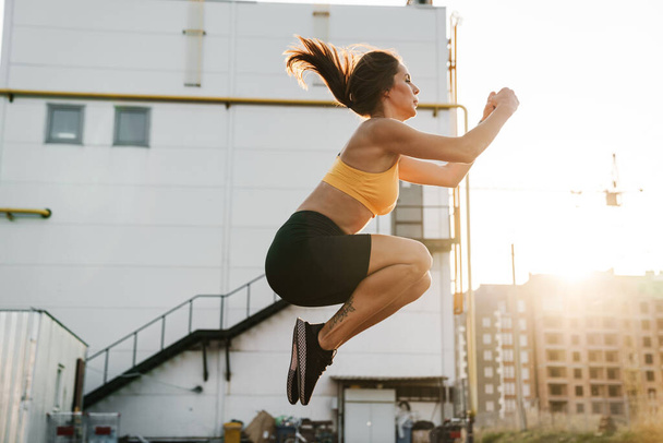 Image of woman in sportswear jumping while doing crunches outdoo - Foto, Bild