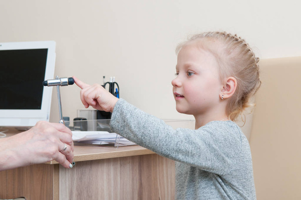 Красива маленька дівчинка робить неврологічний огляд для лікаря з рефлекторним молотком
 - Фото, зображення