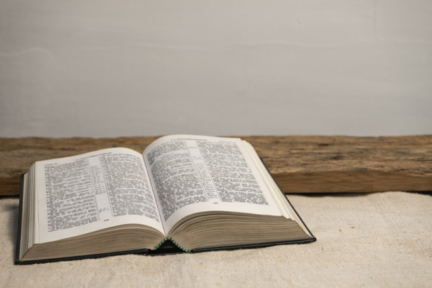 Abre la Sagrada Biblia sobre una vieja mesa de madera y fondo de pared blanco. Concepto de religión
. - Foto, Imagen