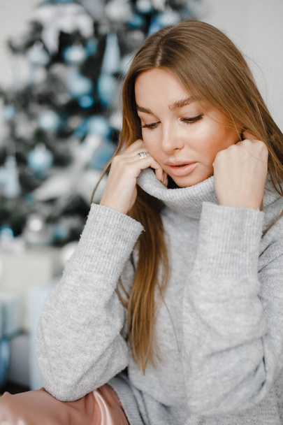 Holidays, celebration and people concept - young woman in elegant in a sweater over christmas interior background - Foto, imagen
