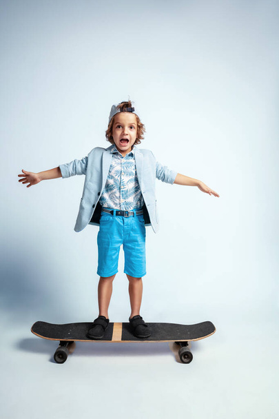 Pretty young boy on skateboard in casual clothes on white studio background - Foto, Imagen