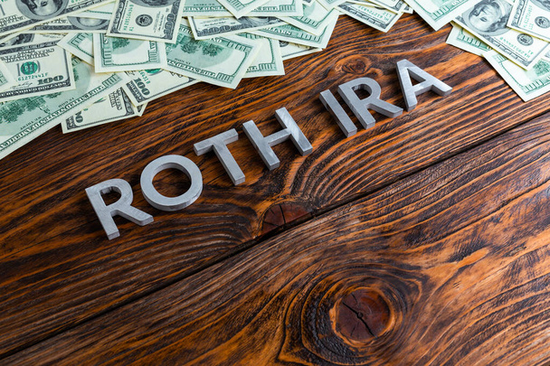 words ROTH IRA laid on wooden surface by metal letters with us dollar banknotes - Photo, Image