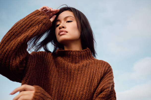 Портрет великолепной азиатской брюнетки в трикотажном свитере чувственно позирует на открытом воздухе
 - Фото, изображение
