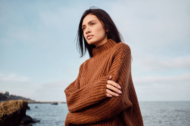 Gorgeous Asian brunette girl in cozy knitted sweater sensually looking away on seaside - Foto, Imagem