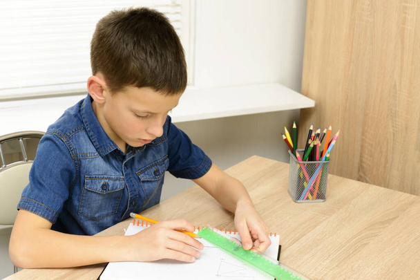 Chico dibujar en el cuaderno. Niño sentado en la casa del escritorio y haciendo su tarea. Escuela, niños, concepto de educación
 - Foto, Imagen