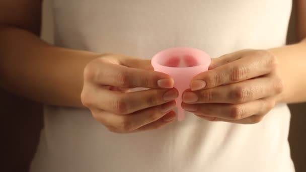 Close up of a young woman in white t-shirt is holding reusable pink silicone menstrual cup  - Materiał filmowy, wideo