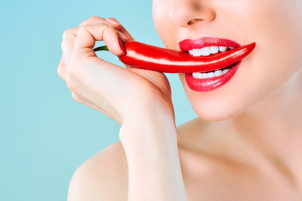 Young woman with chili red pepper isolated en blue background. Sexy female lips. Hot seductive girl - Φωτογραφία, εικόνα