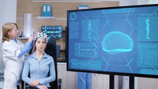 Ekran telewizora z aktywnością mózgu kobiety noszącej skaner mózgu - Materiał filmowy, wideo