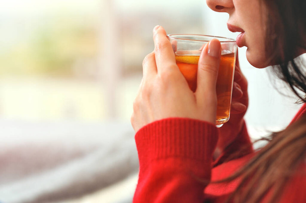 Fiatal nő pihentető tartó csésze citromos tea. Lány álmok néz ki az ablakon. Fiatal nő gondolkodik, miközben otthon citromos teát iszik. - Fotó, kép