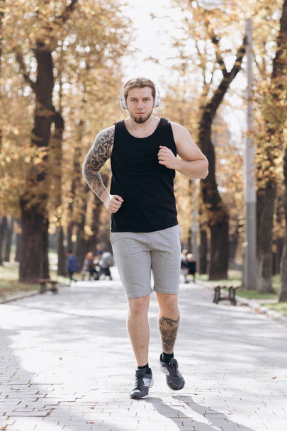 Sport Concept. Athlete Workout For Marathon wearing earphones and listening music. Guy jogging in the park on a background of trees. - Fotó, kép