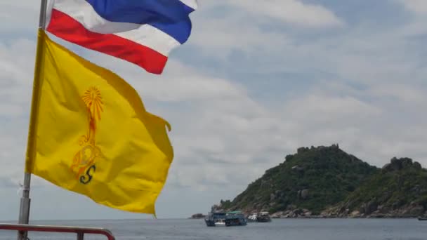 Güneşli tropikal bir günde Tayland bayraklarının yanında yüzen bir tekne. Tayland ve Tayland Kralı 'nın dalgalı denizdeki silueti bulutlu gökyüzüne karşı bir Cennet Koh Tao adası. - Video, Çekim