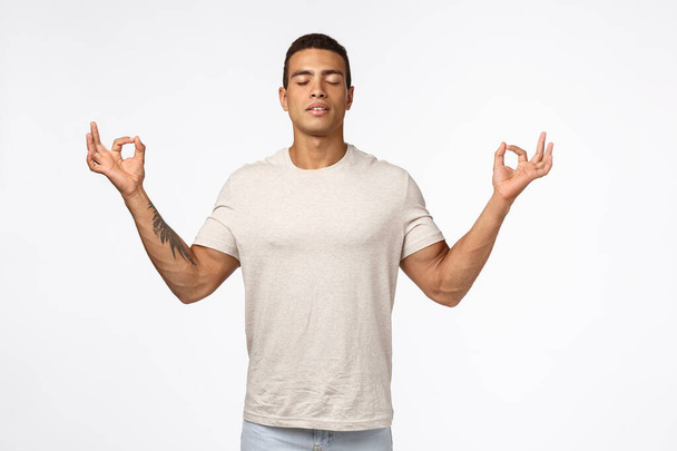 Guy trying find peace in meditation. Musculine handsome young man close eyes, breathe relaxed and patient, spread hands sideways in zen, lotus pose, reach nirvana, practice yoga, white background - Photo, Image