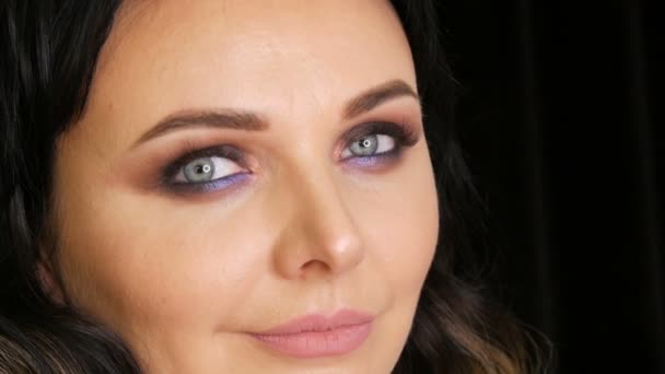 Młoda piękna kobieta z jasnoniebieskimi oczami i wieczornym makijażem wędzone oczy z niebiesko-fioletowym oczkiem na czarnym tle - Materiał filmowy, wideo