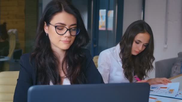 Привлекательная молодая предпринимательница в очках, работающая над ноутбуком в современном офисе
 - Кадры, видео