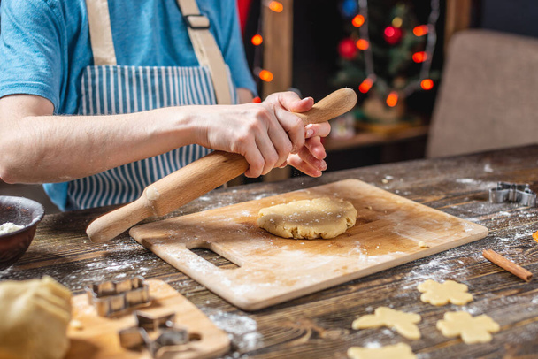 女性はロールピンで生地をロールアウトし、お祝いのジンジャーブレッドを形作ります.クリスマスの時間おいしいクッキーを調理. - 写真・画像