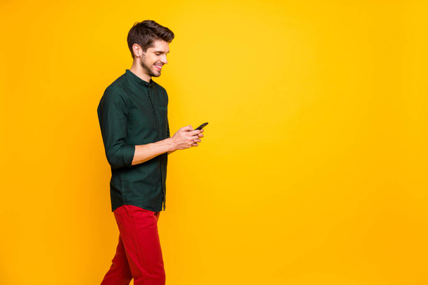 Profile side photo of positive cheerful guy have spring weekends go walk use cellpohne texting followers on social networking blogging wear modern good look clothing isolated shine color background - 写真・画像