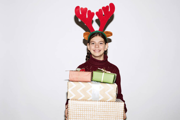 Porträt eines glücklichen Mädchens mit Hirschhörnern, das Geschenkboxen hält und auf weißem Hintergrund isoliert in die Kamera lächelt - Foto, Bild