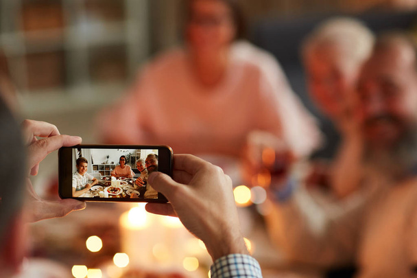 Primo piano dell'uomo che tiene il telefono cellulare e fa foto della famiglia durante la cena in famiglia a casa
 - Foto, immagini