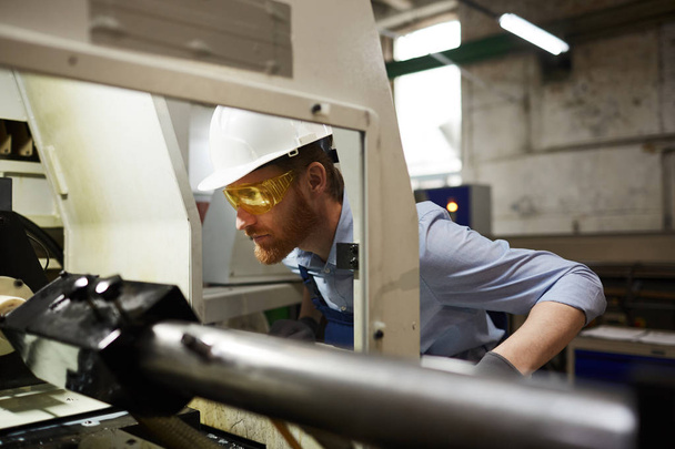 Инженер в камуфляже и защитных очках следит за работой машины на заводе - Фото, изображение