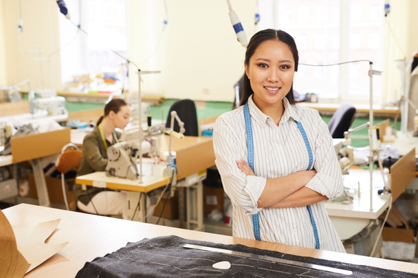 Portrait of Asian young woman smiling at camera while sewing clothing in workshop - Photo, Image