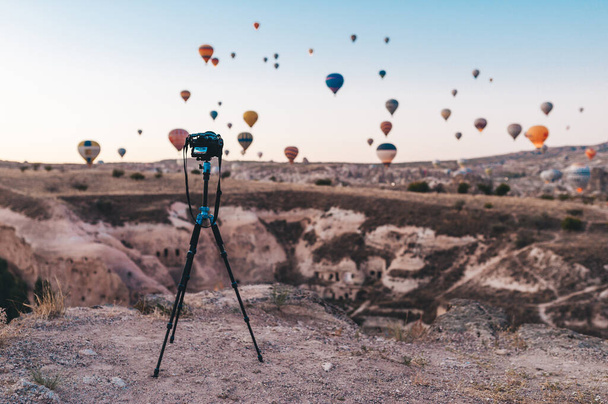 Hot air balloon flying over rock landscape at Turkey. Photo camera on a tripod in the foreground. - Φωτογραφία, εικόνα