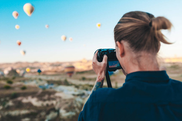 Young man photographer making pictures of air balloons at sunrise time in Cappadocia - Фото, изображение